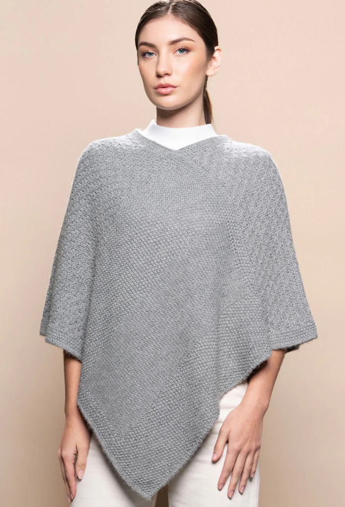 Woman wearing a gray knitted poncho against a beige background