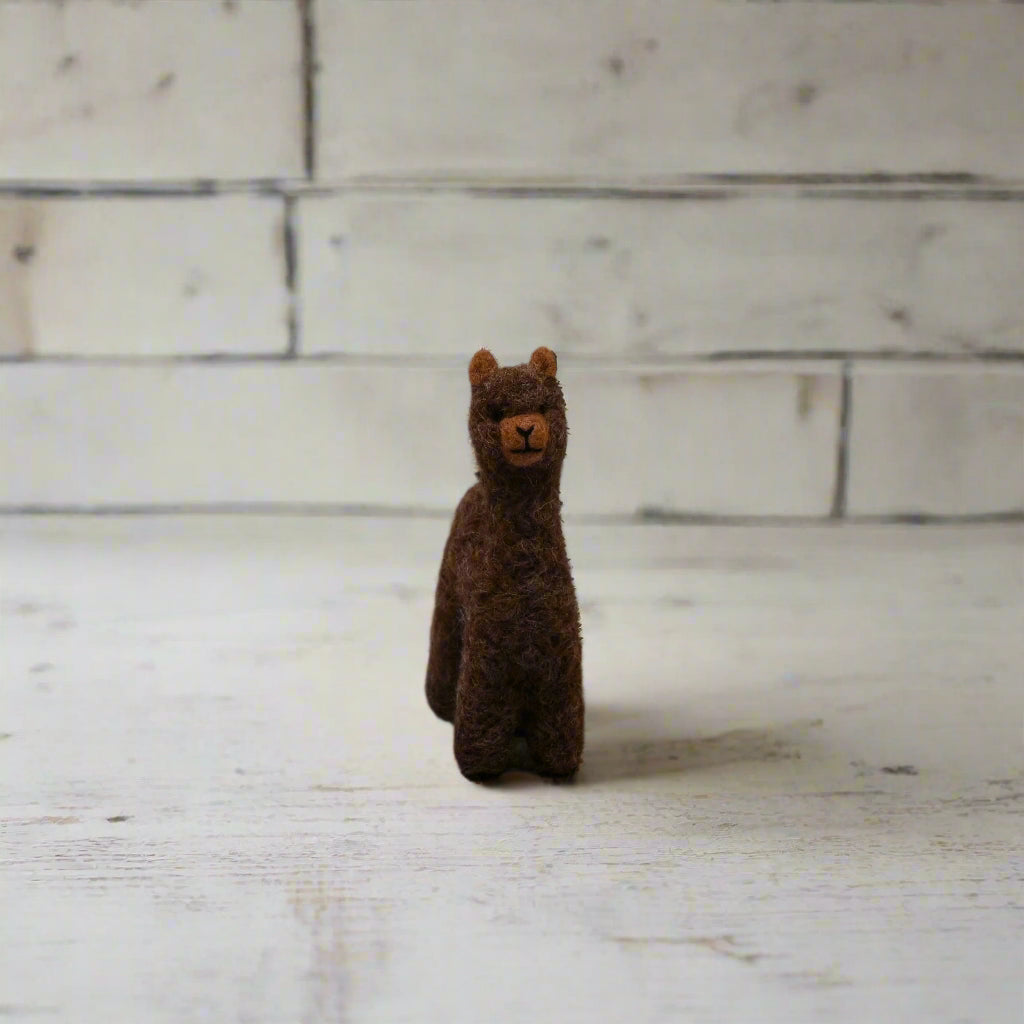 Small brown alpaca figure on a light wooden surface with a white brick wall background