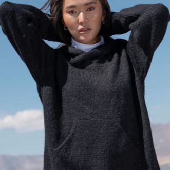 A woman wearing a black long-sleeve pullover with a hood, standing in a scenic outdoor setting.