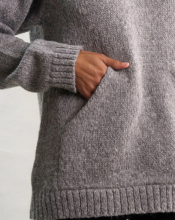 Person wearing a gray sweater with a hand in a pocket against a light background