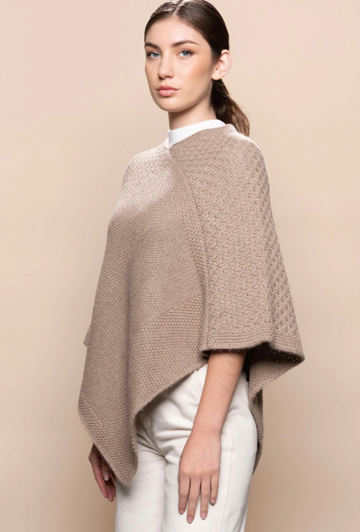 Woman wearing a beige knitted poncho against a beige background