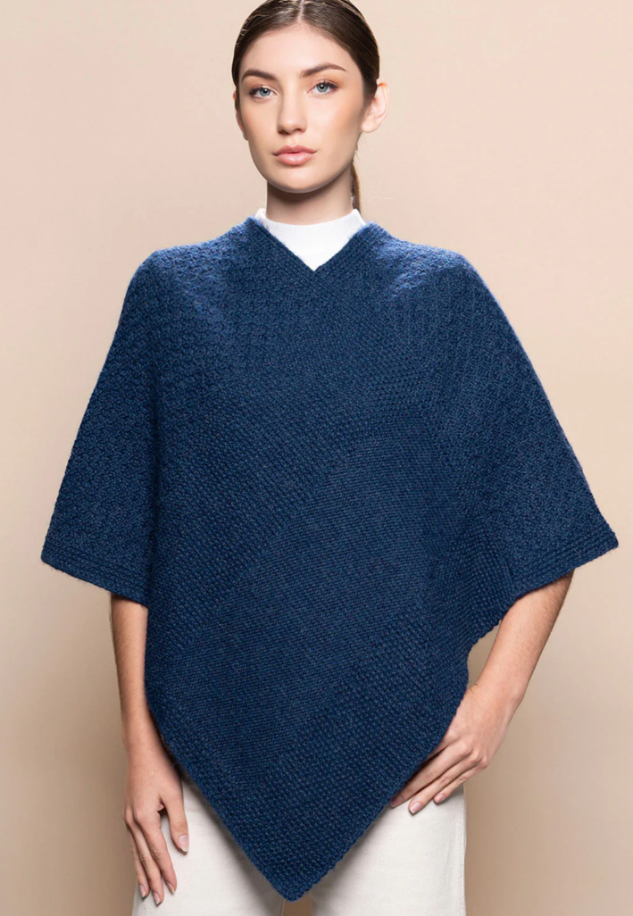 Woman wearing a blue knitted poncho against a beige background